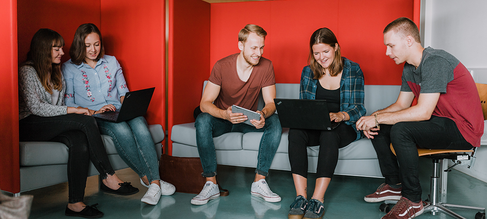 Studierende sitzen auf Sofas im Mobile Lab und arbeiten gemeinsam an Laptops und Tablet.