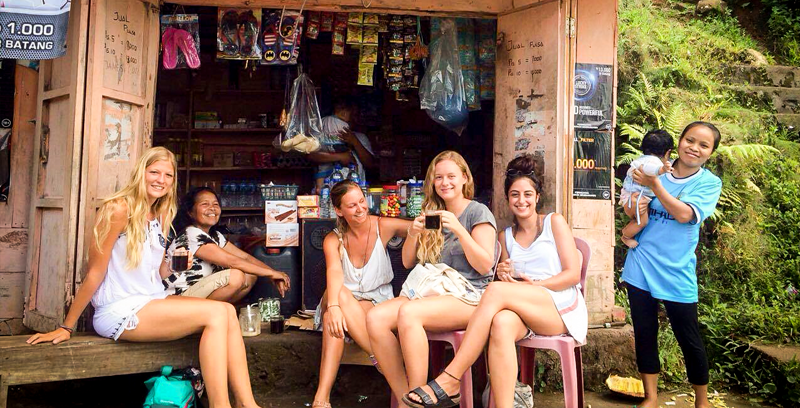 Studentin sitzt mit Einheimischen und ihren Freundinnen vor einem kleinen Holzkiosk am Straßenrand in Flores Indonesien.