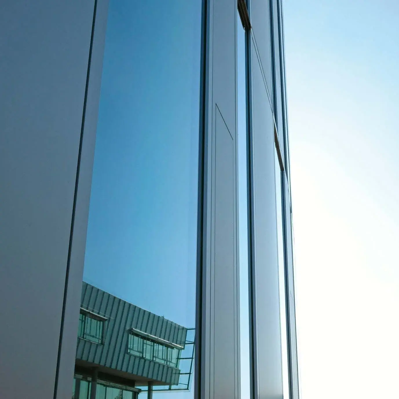 Close-up of a university building, with the main building reflected in its windows.