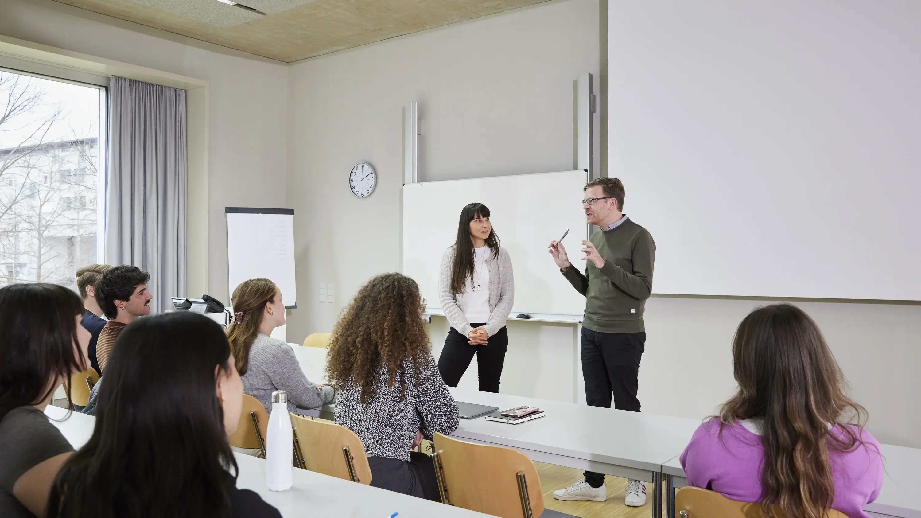 A student and a professor are talking during a lecture at his desk.