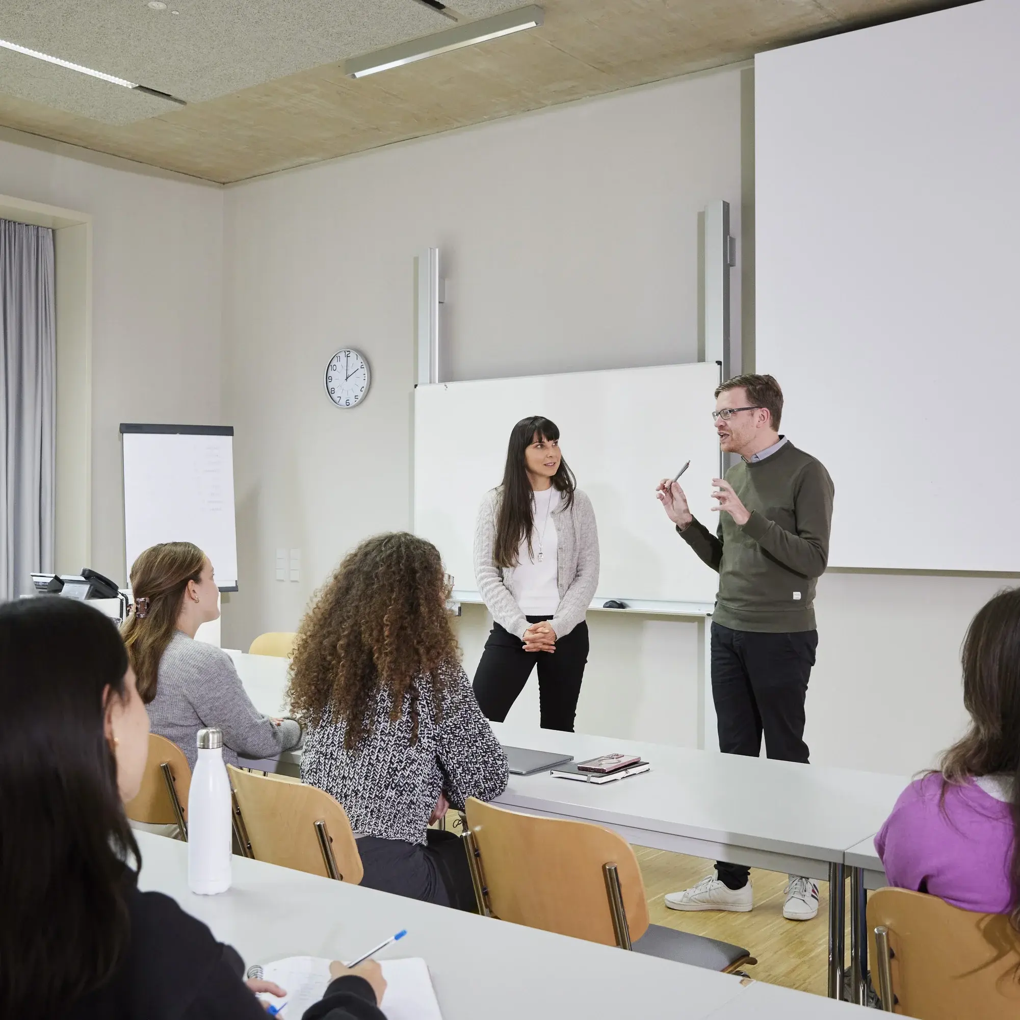 A student and a professor are talking during a lecture at his desk.