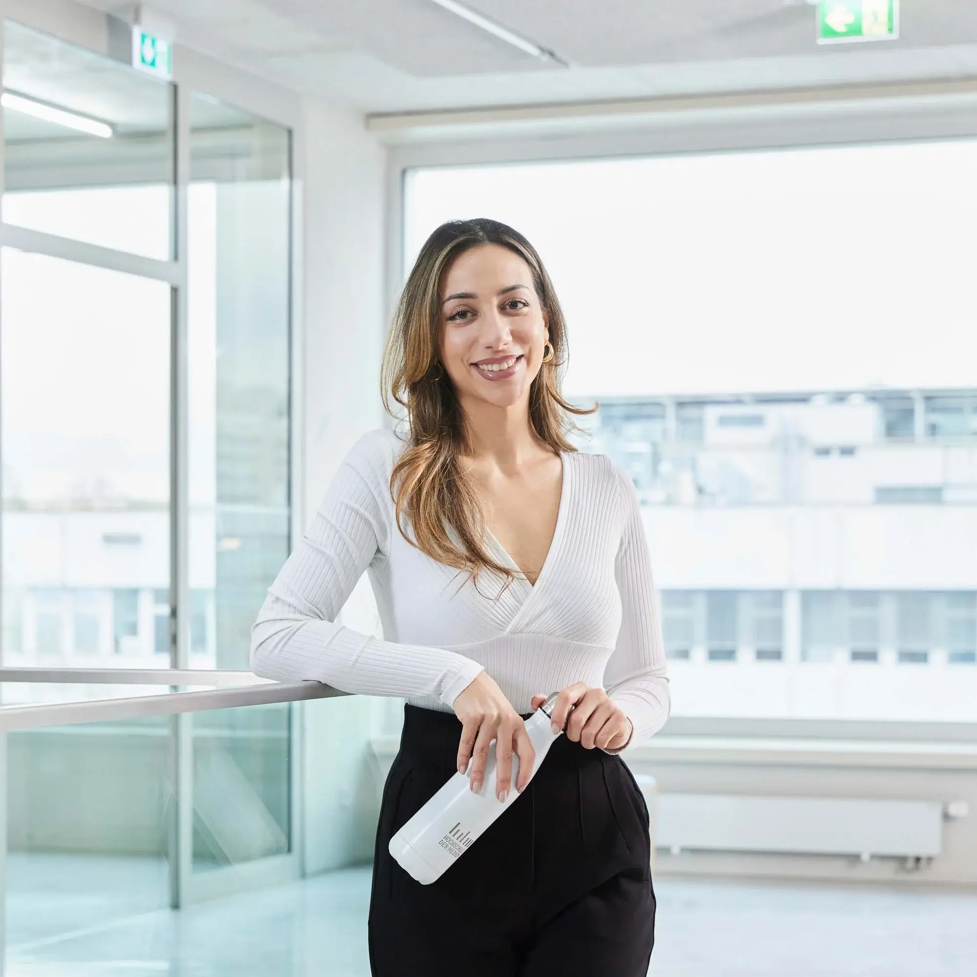 A student stands with her water bottle in the hallway of the Hochschule der Medien.