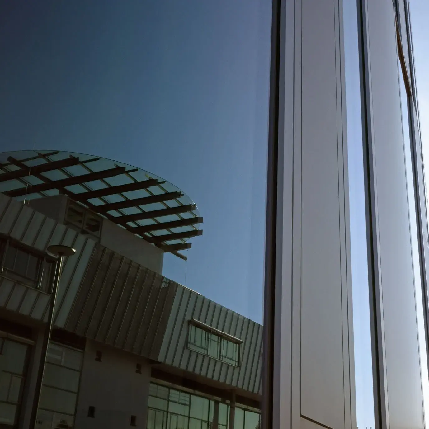 Nahaufnahme eines Hochschulgebäudes, in dessen Fenster sich das Hauptgebäude spiegelt.