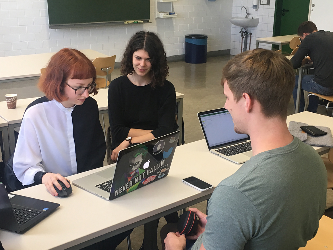 drei Studierende sitzen um einen Tisch mit einem Laptop und führen Benutzertests durch.