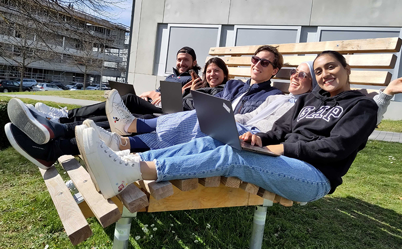 Studierende sitzen zusammen auf der Bank vor dem Gebäude "Würfel" an der Hochschule der Medien.